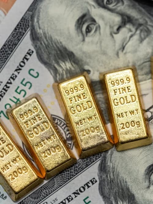 Five 999.9 fine gold bars resting on hundred-dollar bills